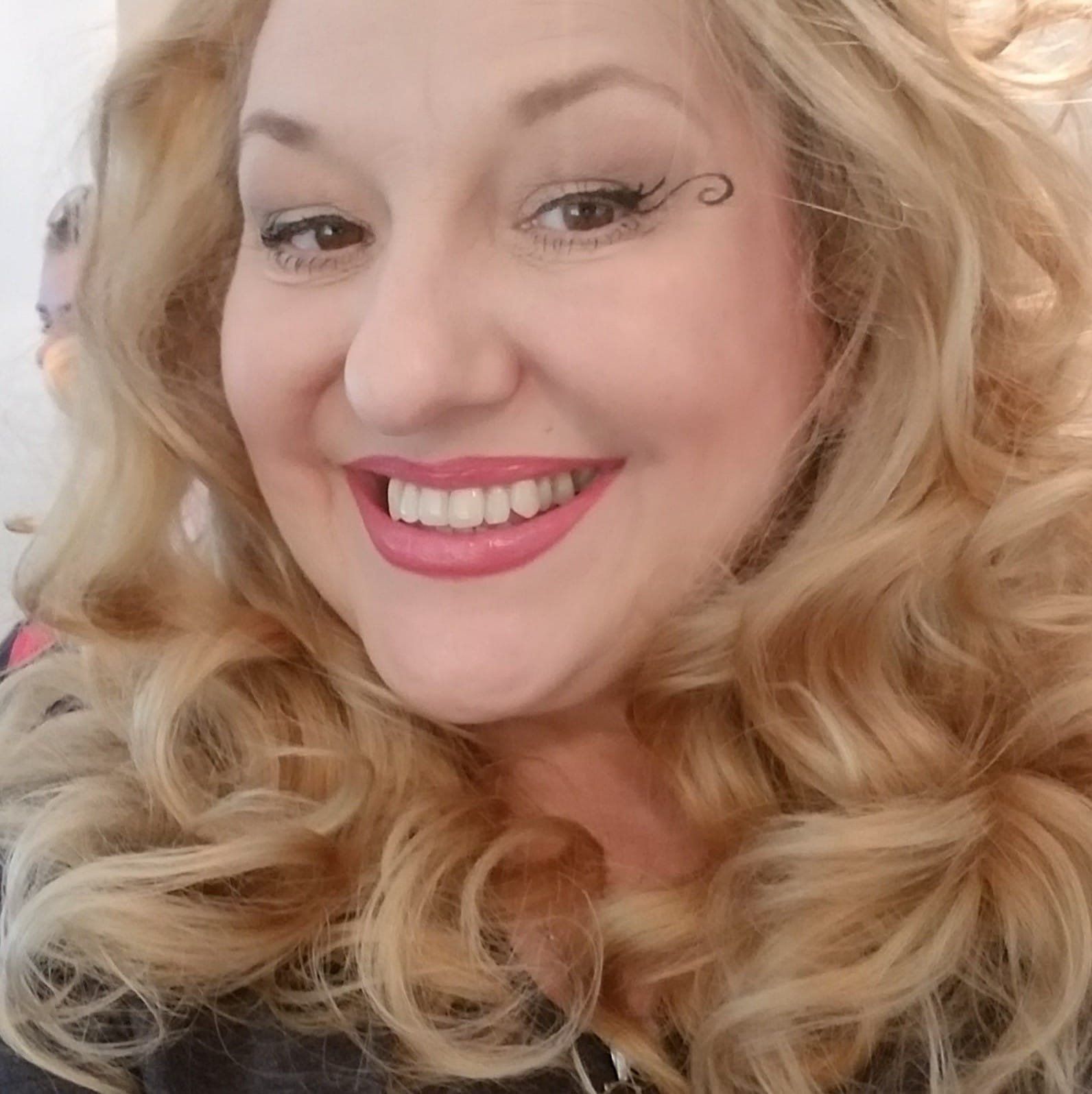 A woman with blonde hair is smiling with a tattoo on her forehead, Belladonna LaVeau.