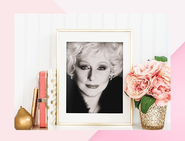 A black and white photo of a woman is sitting on a table next to a vase of flowers, Mary Kay.