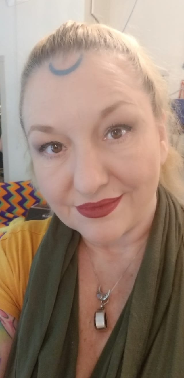 A woman with a tattoo on her forehead is wearing a scarf and a necklace, Belladonna LaVeau.