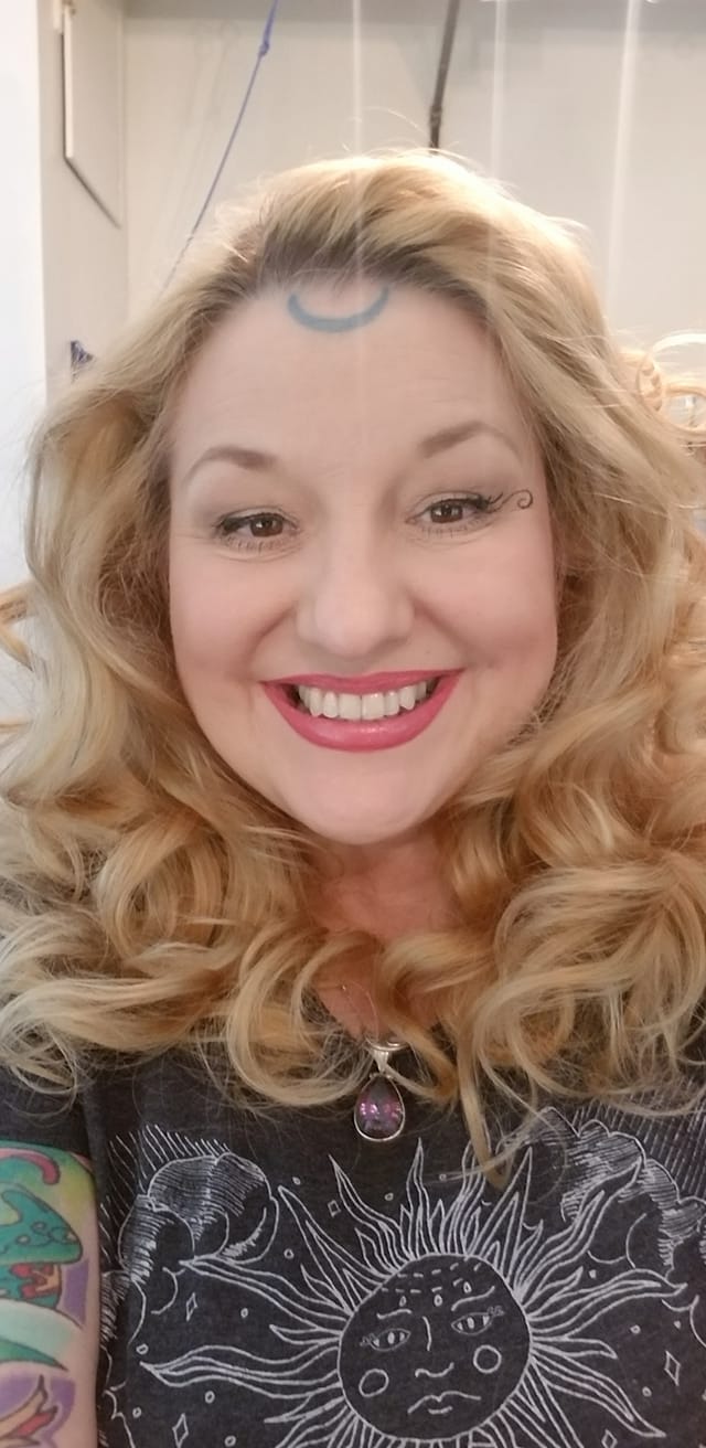 A woman with blonde hair and a tattoo on her forehead is smiling, Belladonna LaVeau.