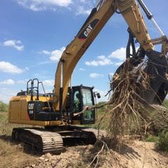 A cat excavator is scooping roots out of a pile of dirt.