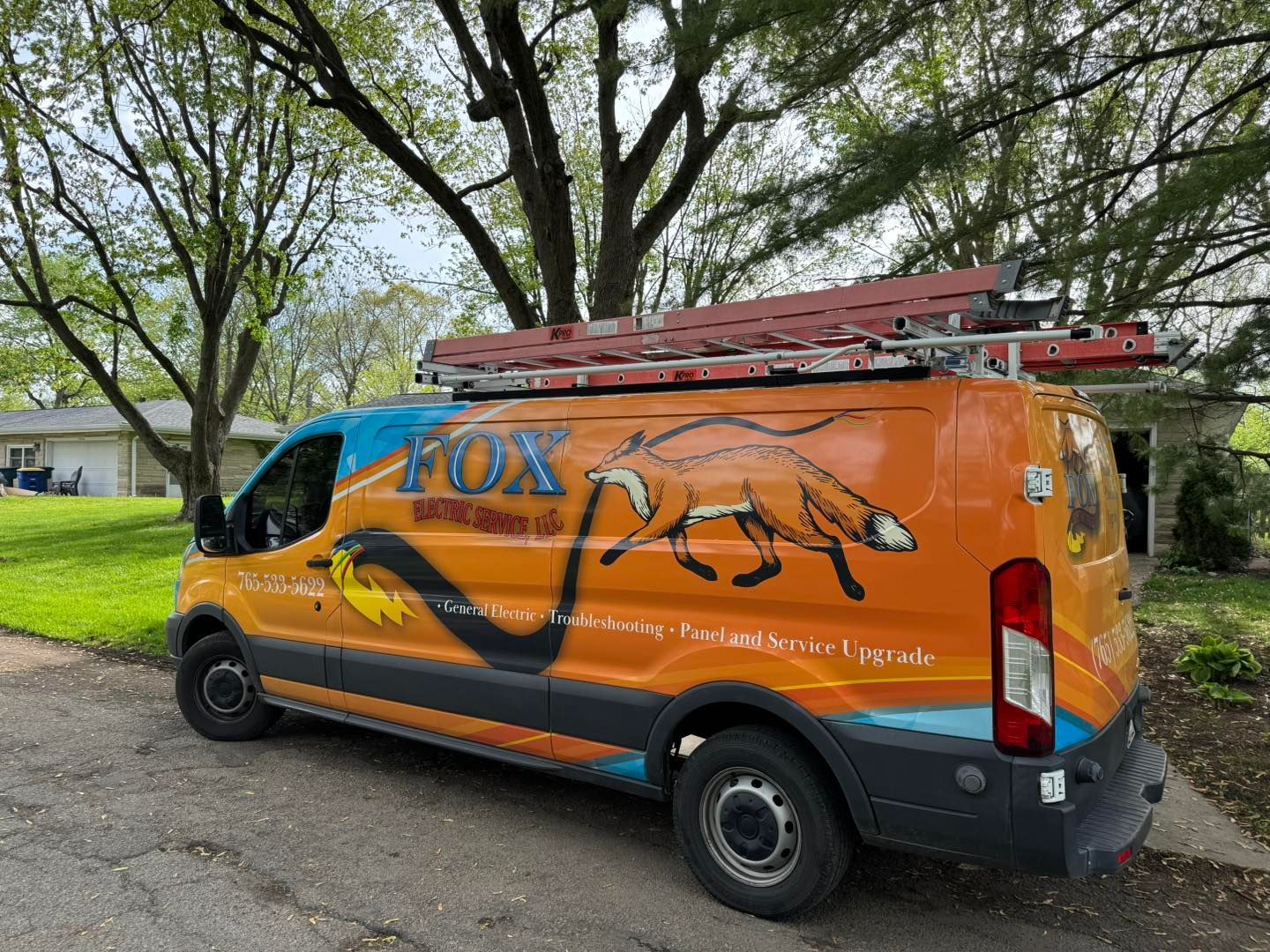 An orange van with a ladder on top of it is parked on the side of the road.