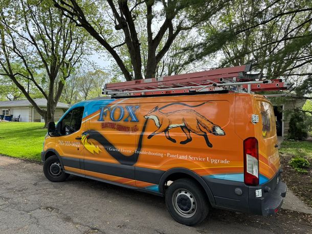 An orange van with a ladder on top of it is parked on the side of the road.