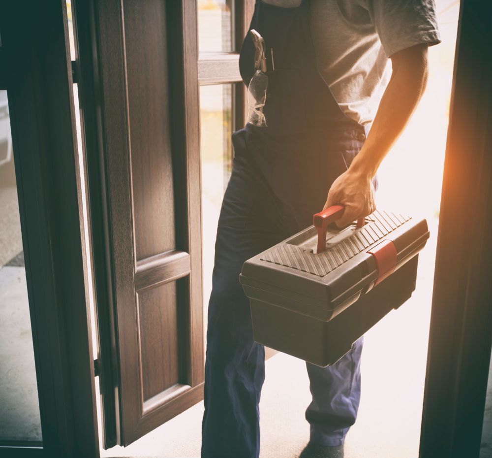A man is carrying a toolbox into a doorway.