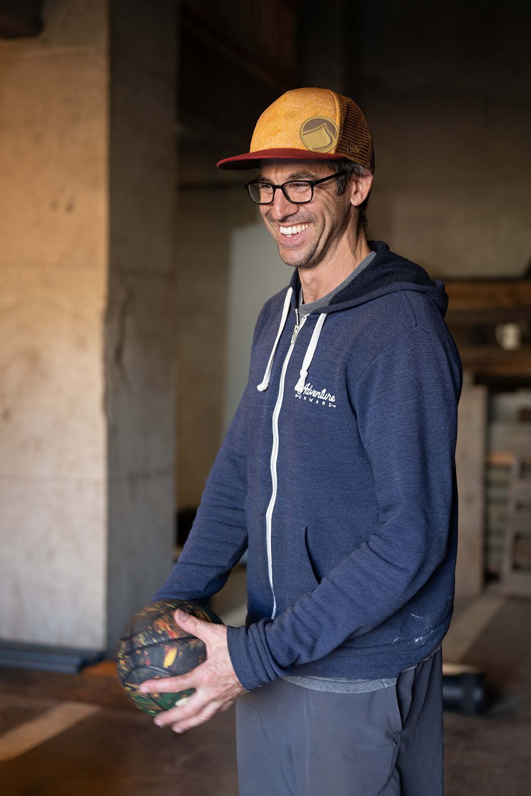 A man wearing a hat and glasses is holding a bowling ball.