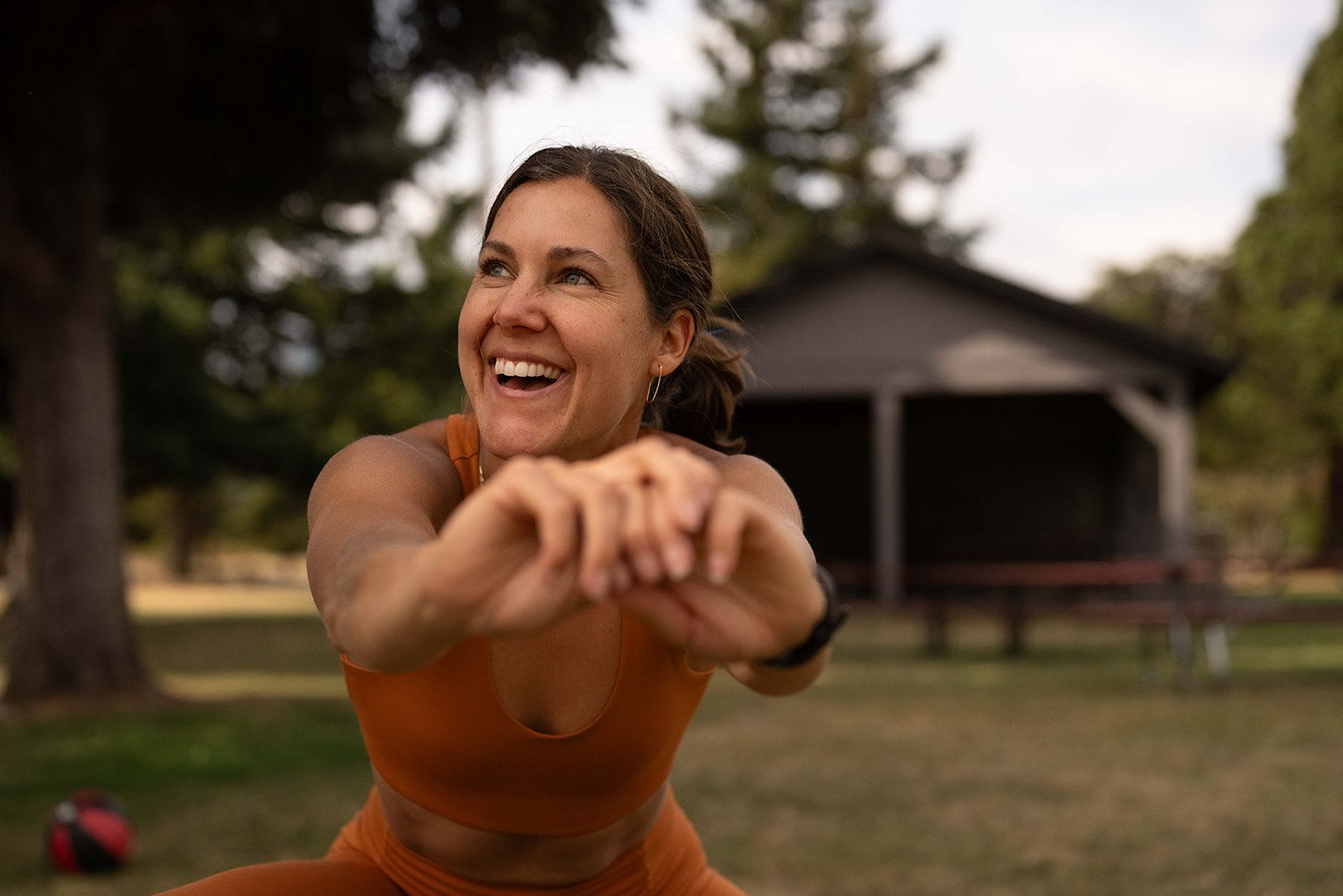 A woman is smiling while doing squats in a park.