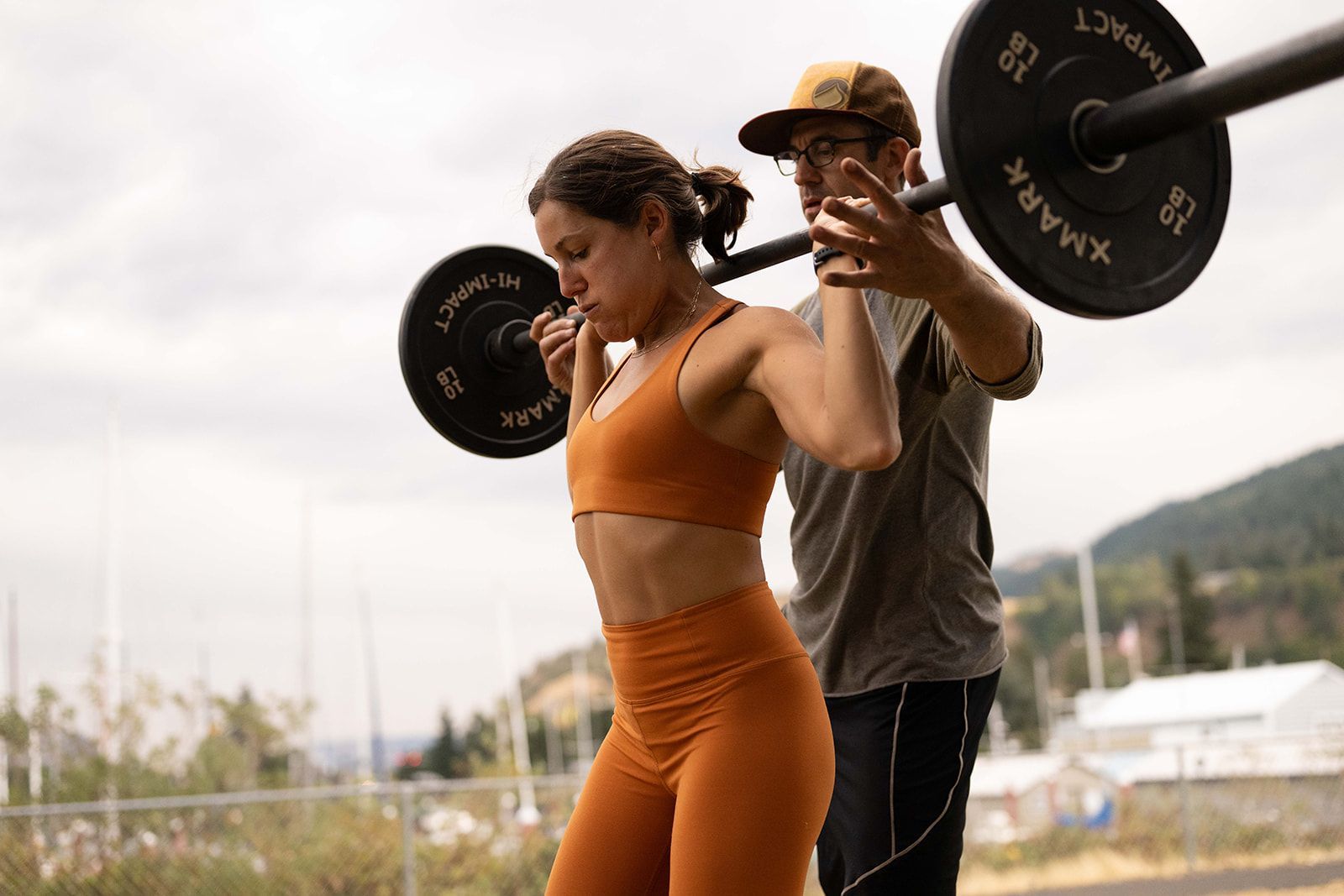 A man is helping a woman squat with a barbell.