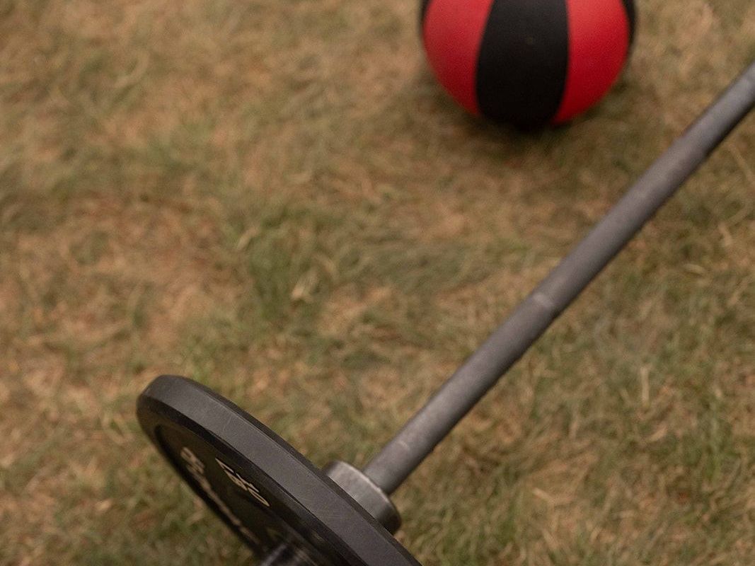 A red and black ball is sitting next to a barbell on the grass.