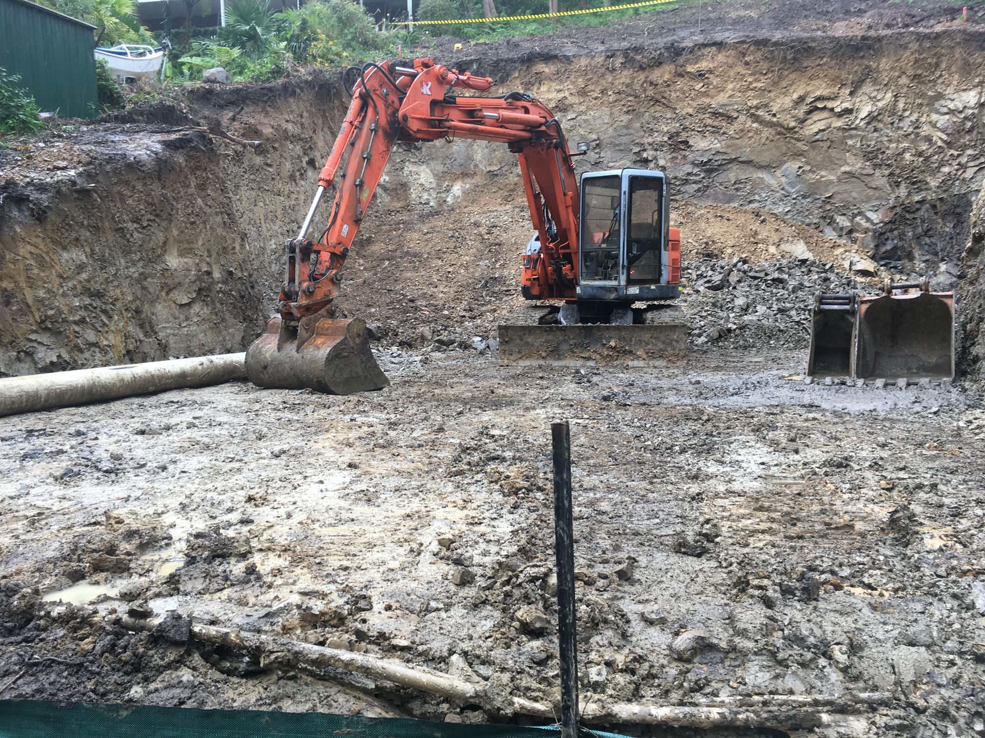 Orange excavator in a muddy construction site, digging into a dirt bank. — Lakesway Earthmoving in Charlotte Bay, NSW
