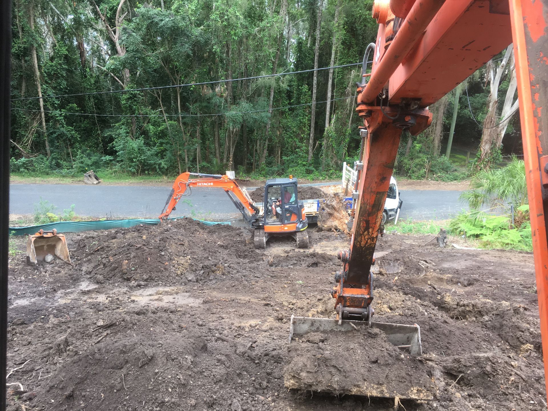 Construction site with excavators digging dirt near a road and trees; orange and green machinery, overcast day. — Lakesway Earthmoving in Charlotte Bay, NSW
