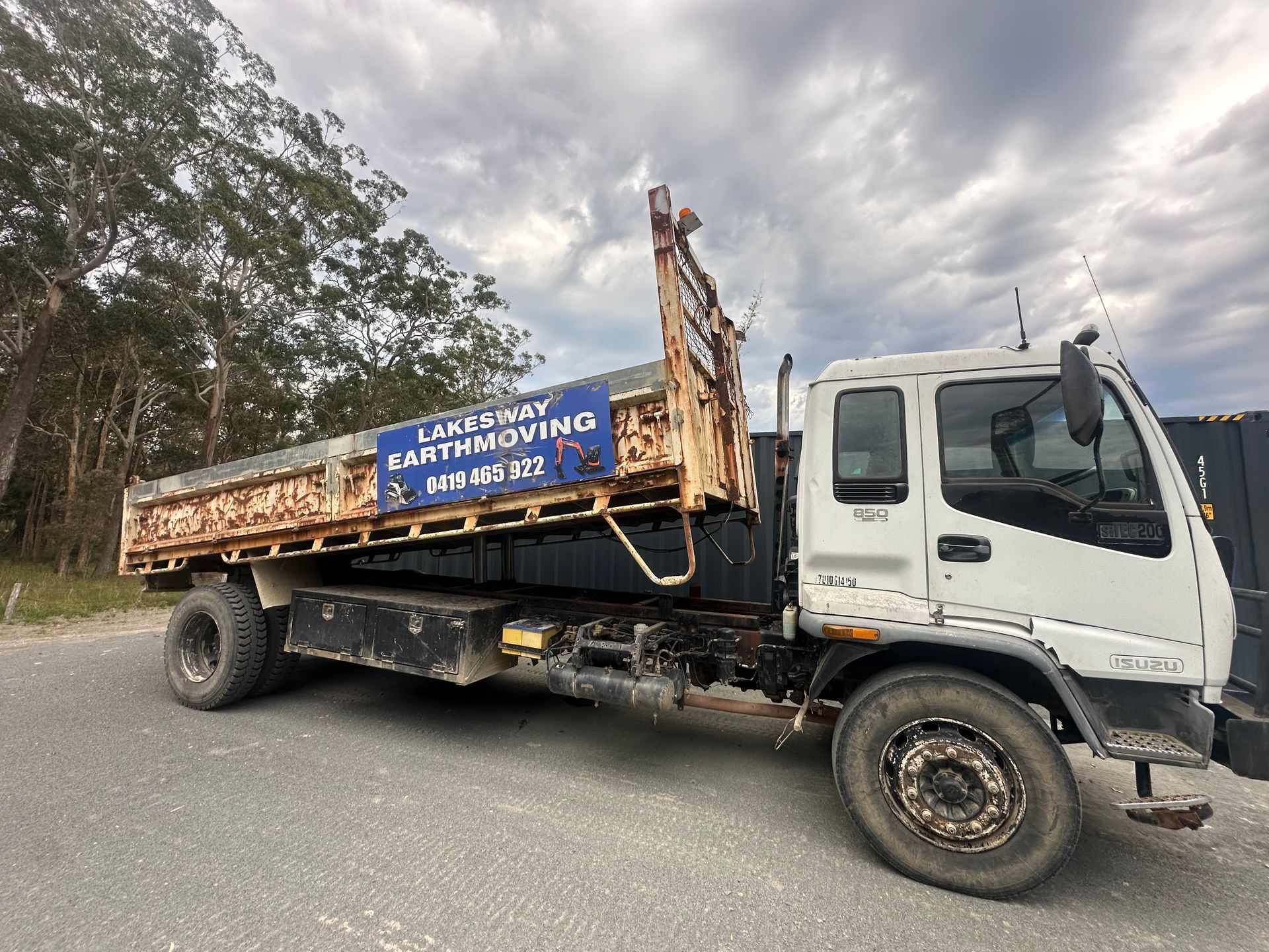 White flatbed truck with rust, parked on gravel, cloudy sky. — Lakesway Earthmoving in Charlotte Bay, NSW