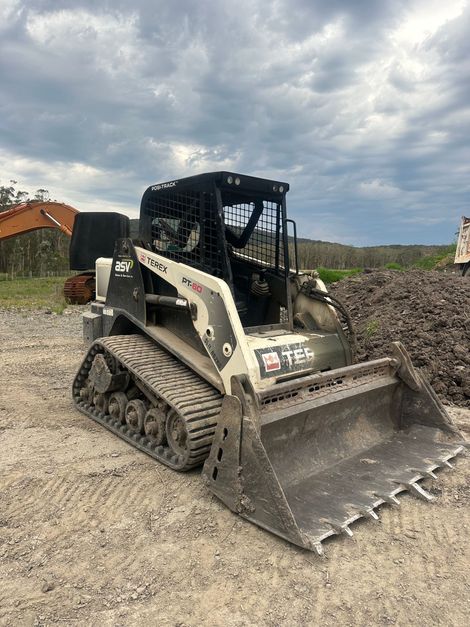 A black and white skid steer loader on a gravel surface with a cloudy sky in the background.