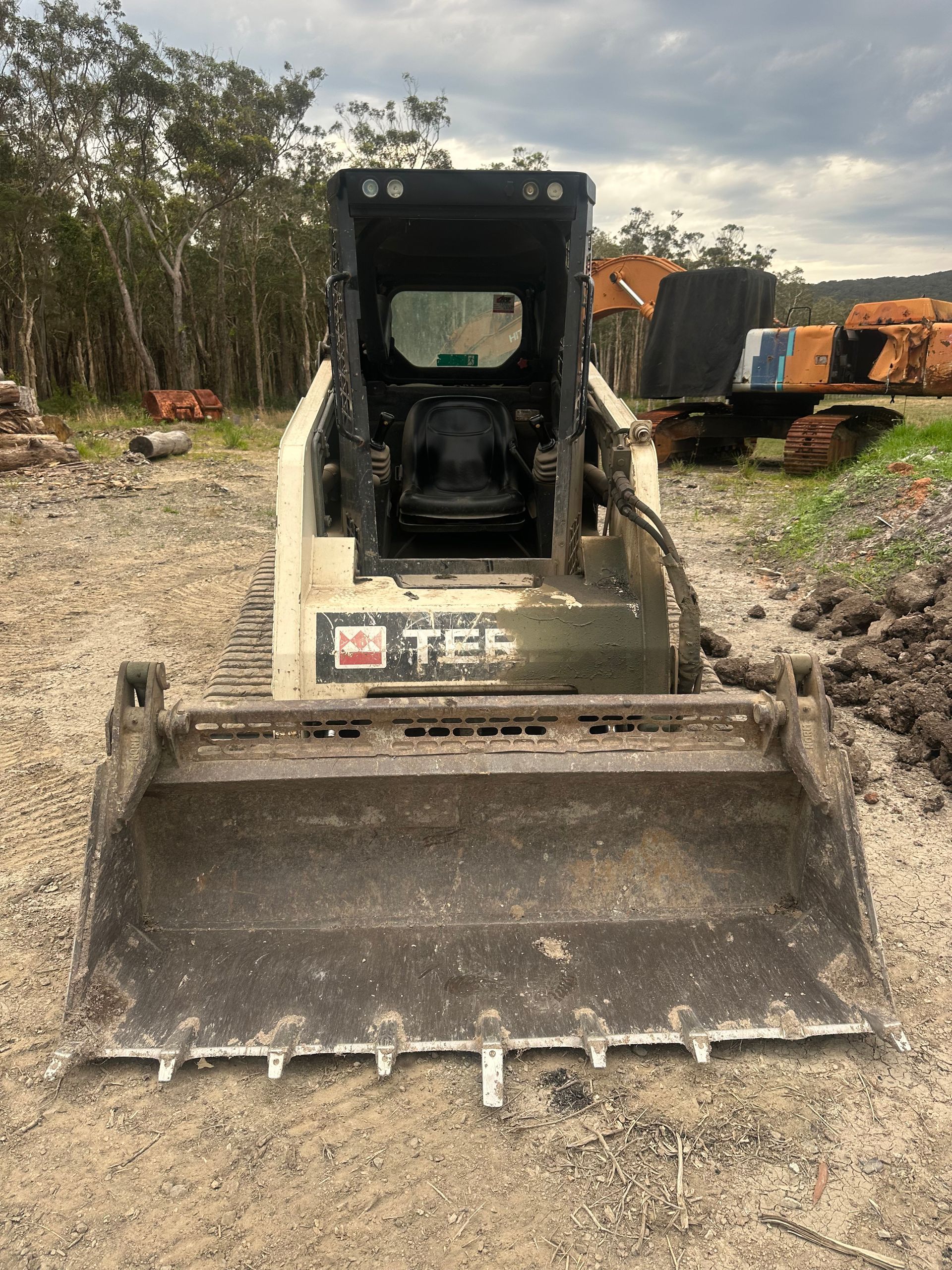 Skid steer loader with a front bucket on a gravel surface. The machine is white and black. — Lakesway Earthmoving in Charlotte Bay, NSW