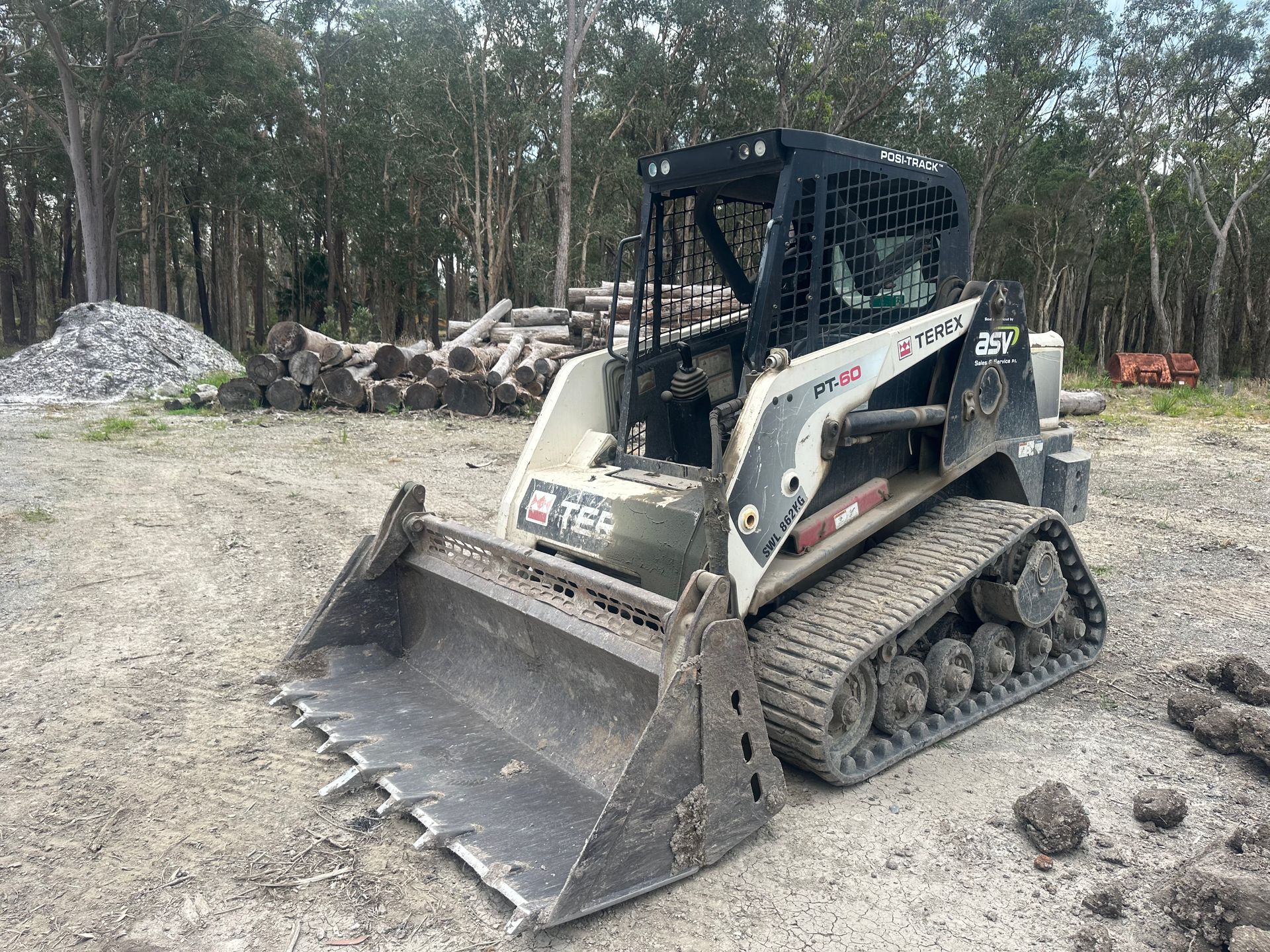Bobcat track loader with bucket in a gravel area with logs and trees in the background. — Lakesway Earthmoving in Charlotte Bay, NSW