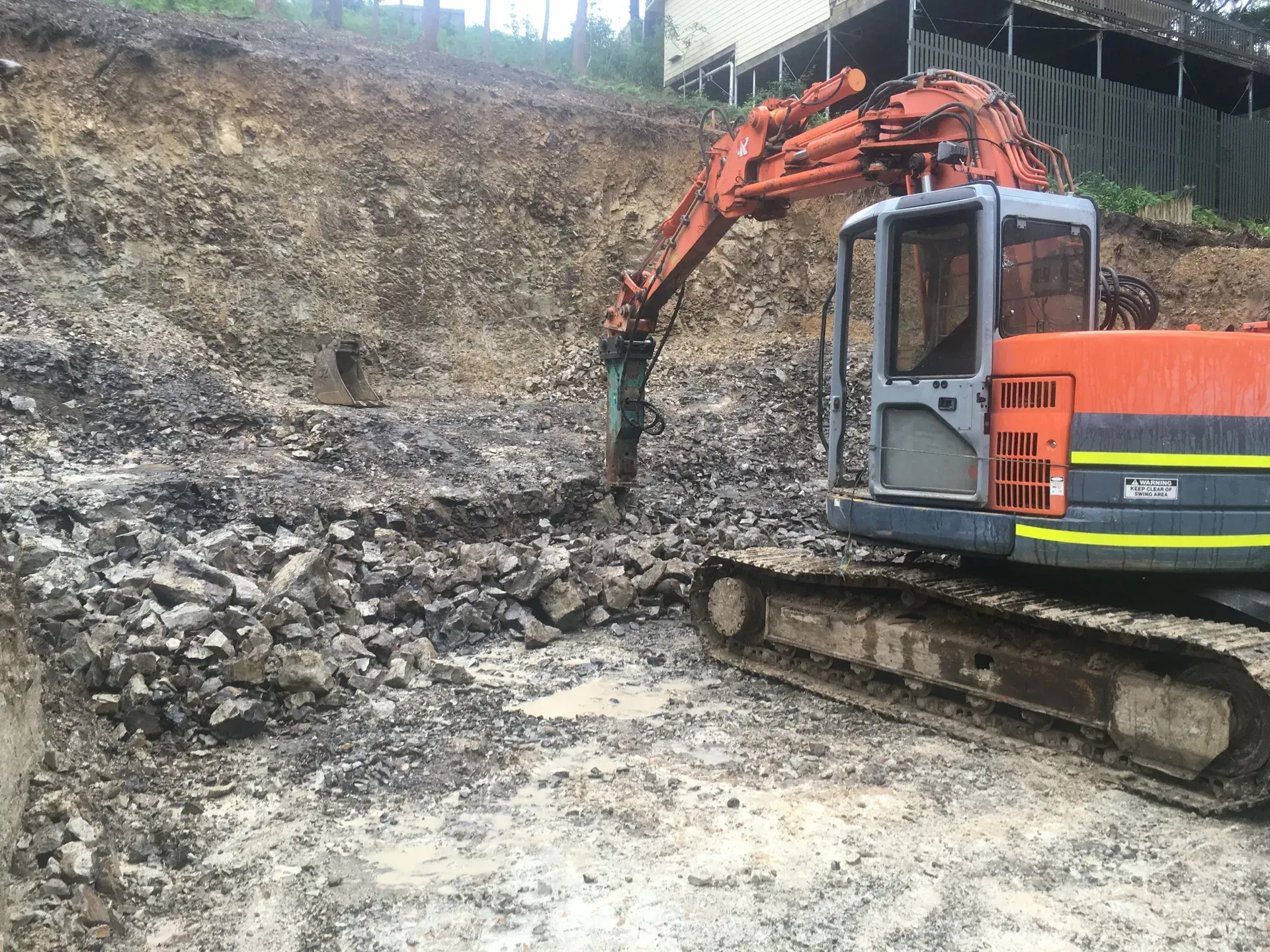 Excavator breaking rock on a construction site, digging into a dirt hill. — Lakesway Earthmoving in Charlotte Bay, NSW