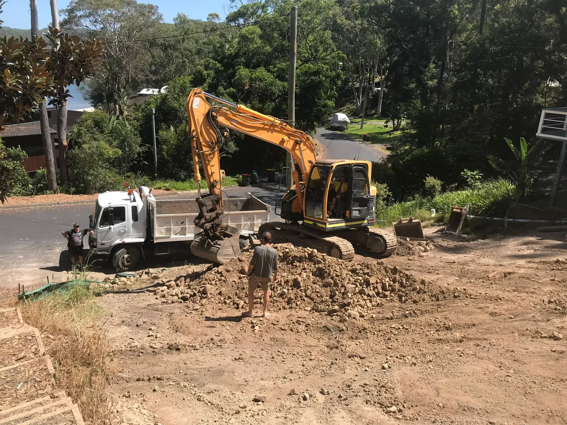 Yellow excavator loading dirt into a white dump truck, next to a road. — Lakesway Earthmoving in Bulahdelah, NSW