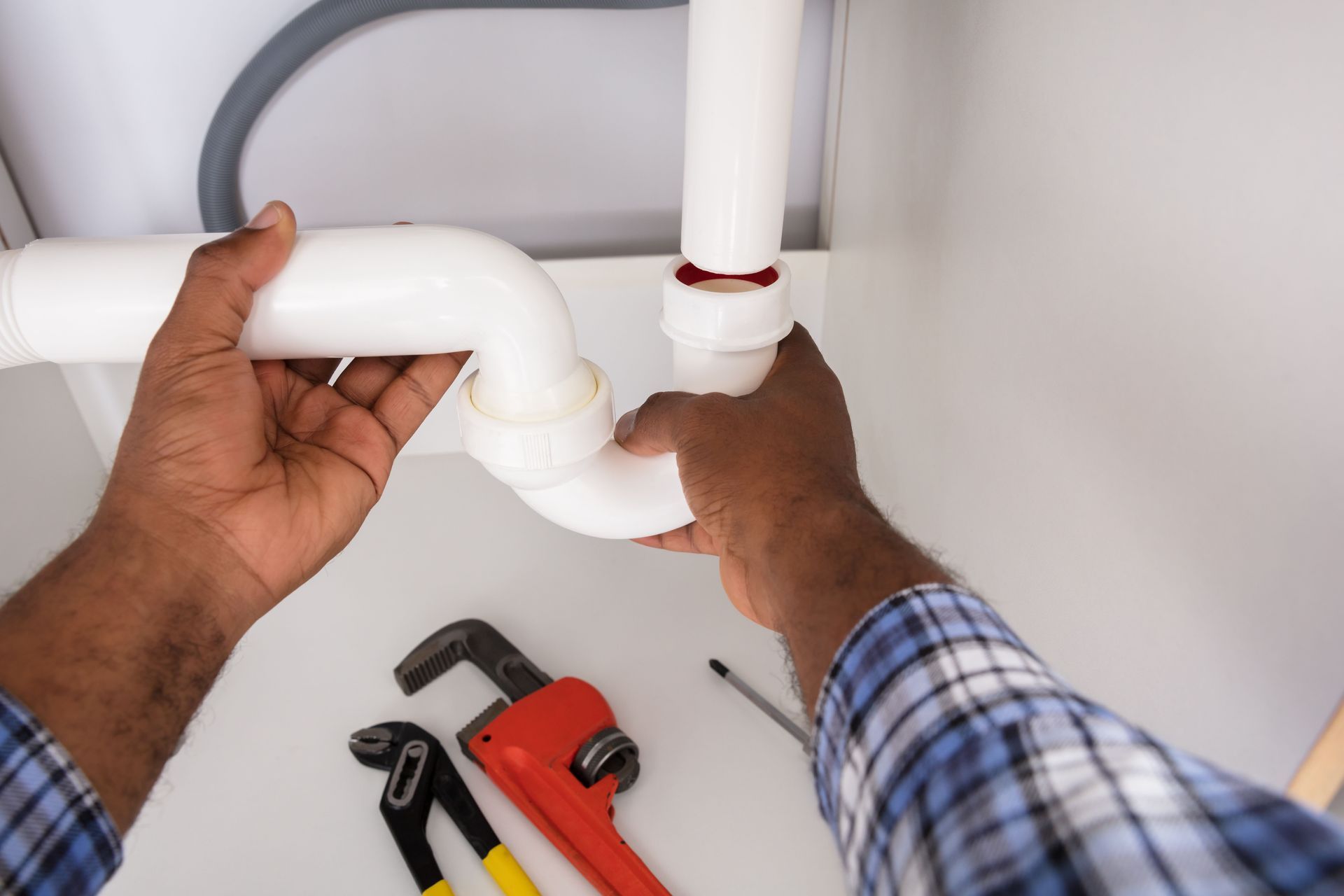 Hands assembling a white plastic sink drainpipe under a white sink.