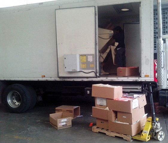 Una pila de cajas de cartón se encuentra junto a un camión blanco.