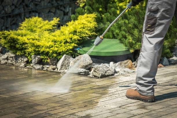 A person is using a high pressure washer to clean a wooden deck.