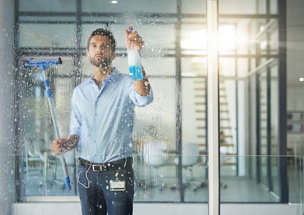 Guy cleaning window with cleaner in his left hand and a squeegee device with his right hand 