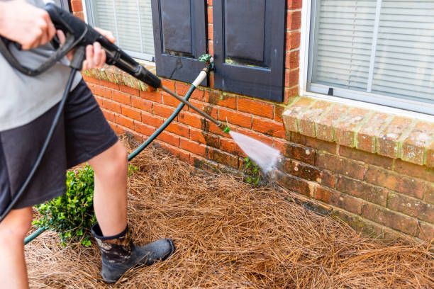 A person is using a high pressure washer to clean a brick wall.