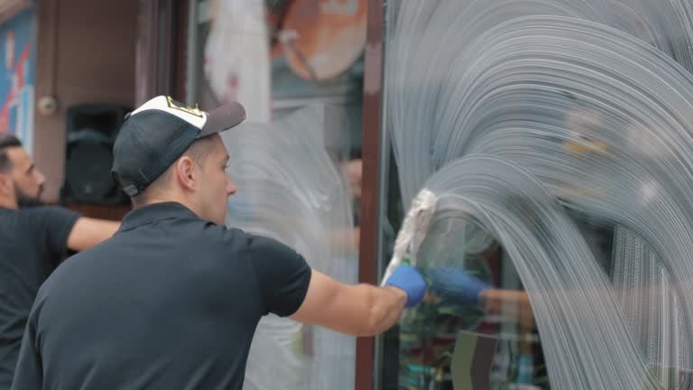 Two men is cleaning a window with a squeegee, with lots of soap