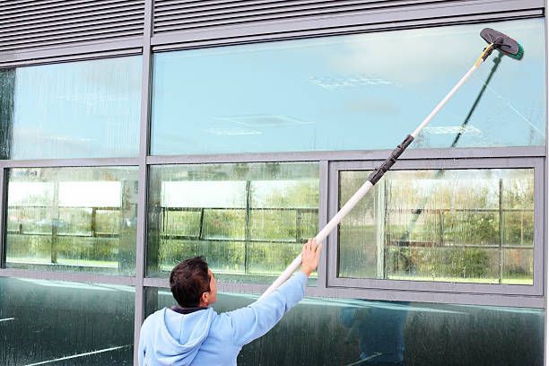 A man is cleaning a window with a long pole.