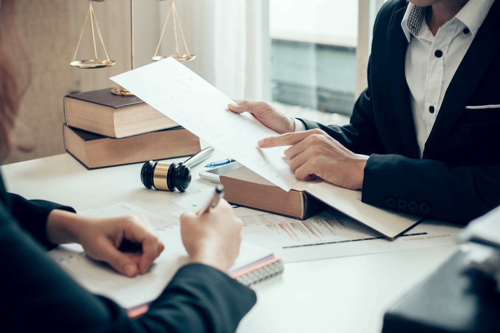 Two people reviewing legal documents at a desk with gavel and scales.