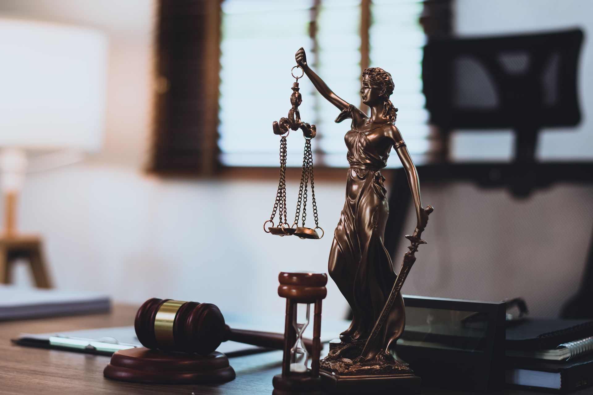 A Lady Justice statue stands beside a gavel and hourglass on a law office desk. A Lady Justice statue stands beside a gavel and hourglass on a law office desk.