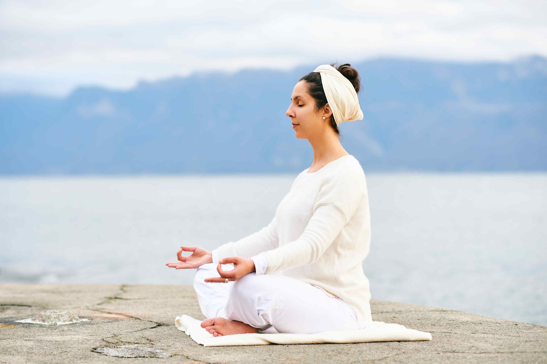 Woman wearing whit siting on a white towel performing Kundalini Rebirthing