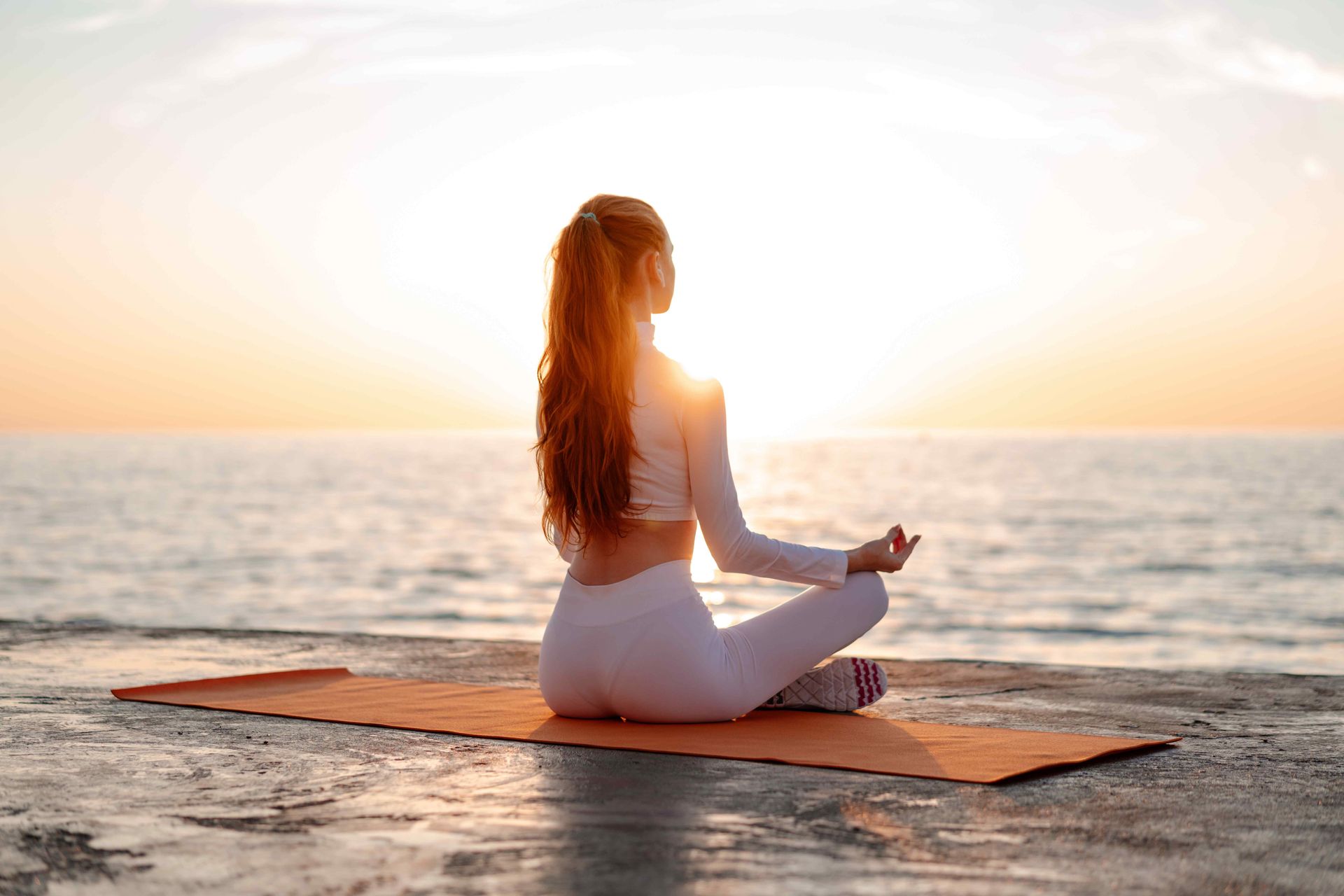 woman sitting on a yoga map performing a yoga pose with the sun set in the background