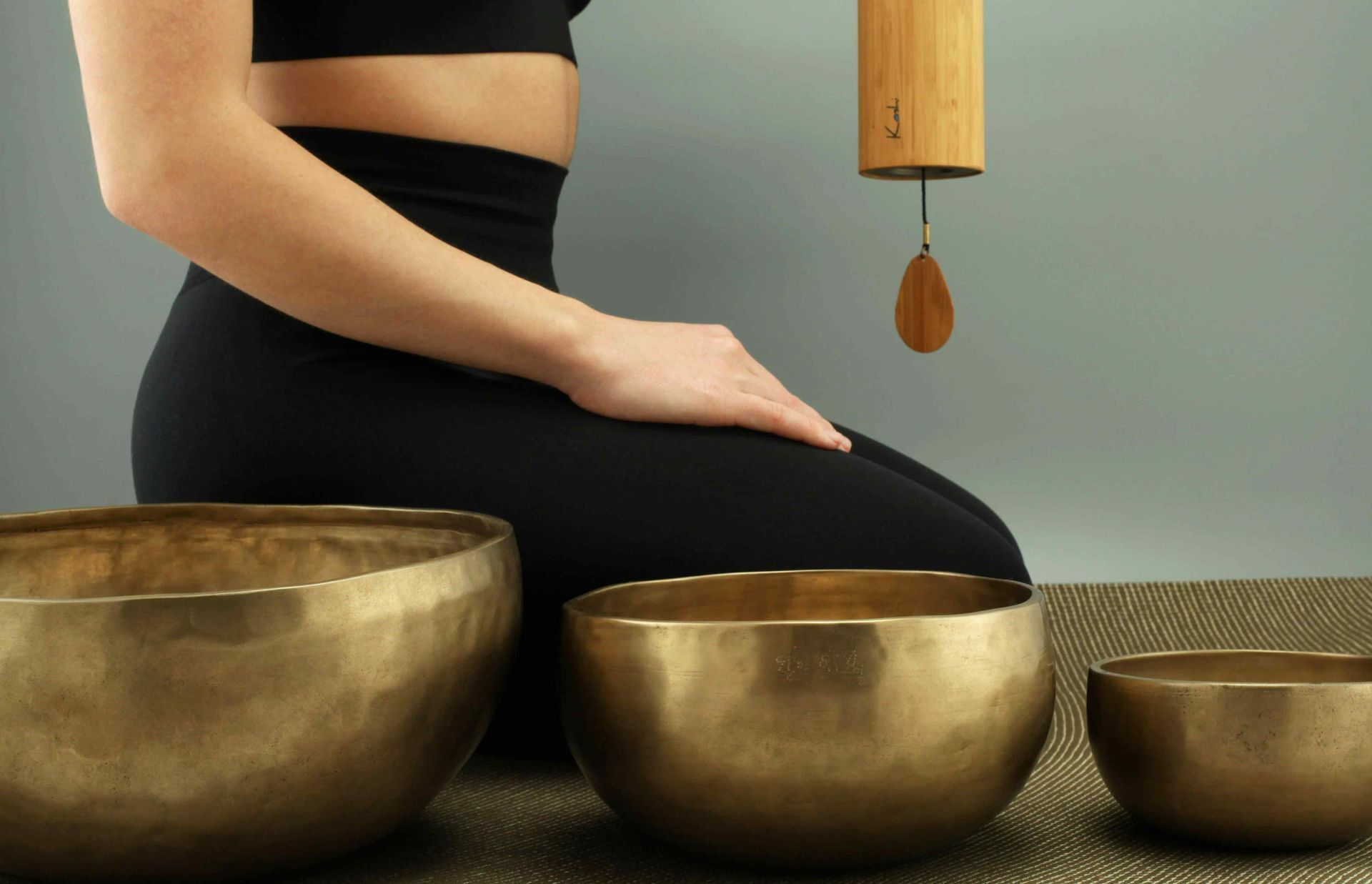 A woman sits on a mat with 3 copper vibroacoustic therapy bowls beside her.