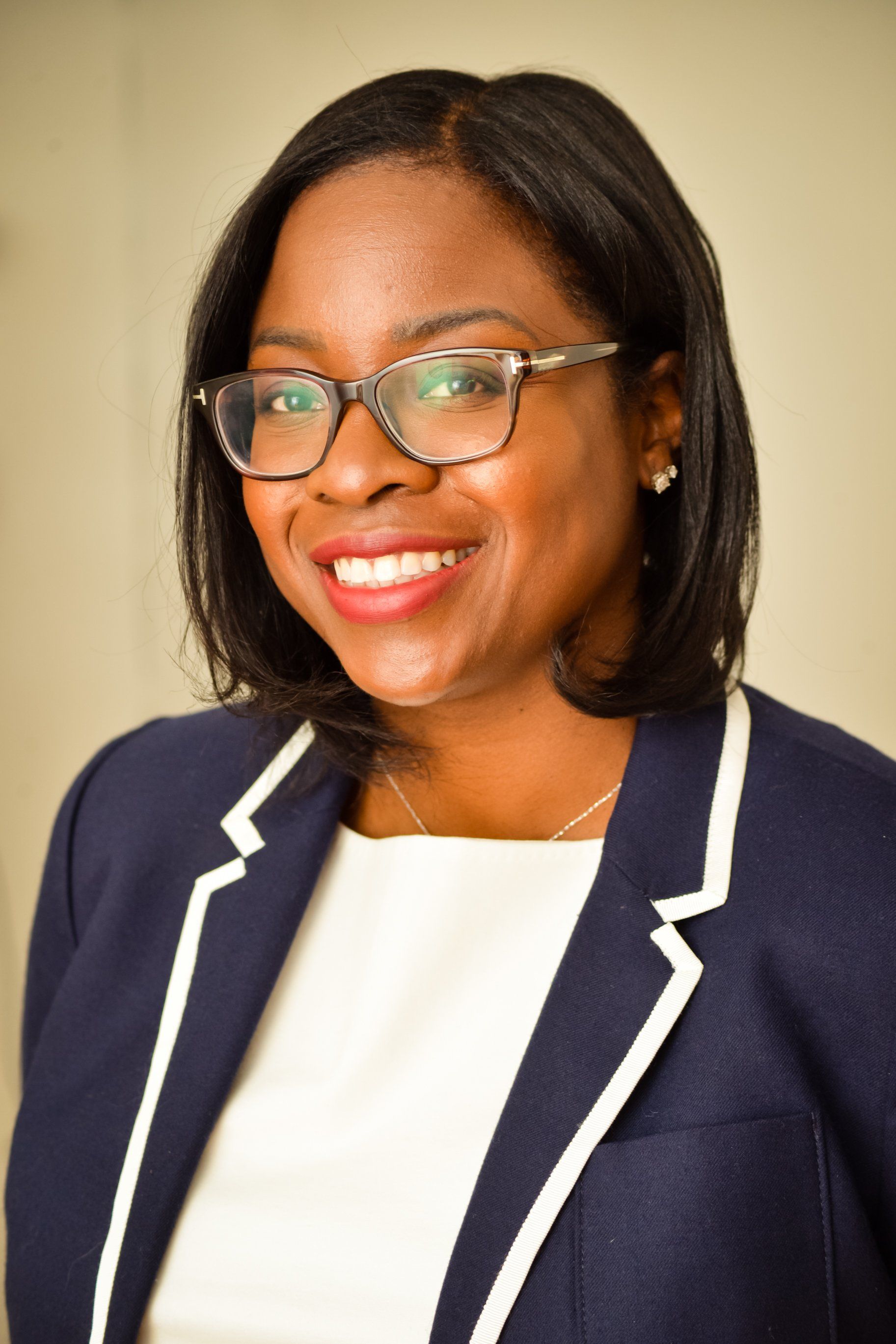 A woman wearing glasses and a blue jacket is smiling for the camera.