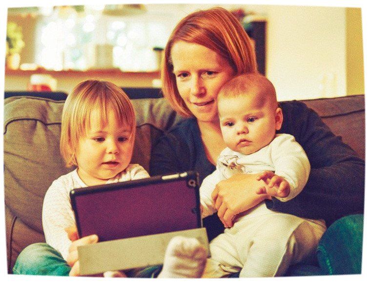 Women sat on sofa looking at a tablet with 2 small children on her lap. Return to work coaching for professionals to return to the workplace with confidence, clarity and conviction.