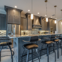 A kitchen with a large island , stools and a refrigerator.