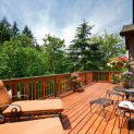 A wooden deck with chairs , tables and a railing surrounded by trees.