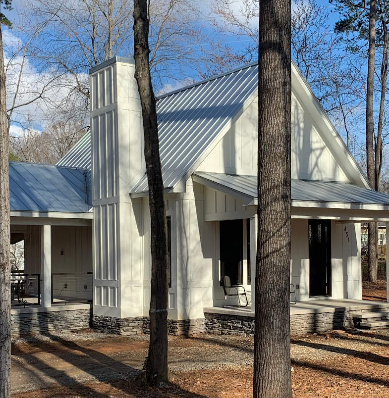 A white house with a metal roof is surrounded by trees