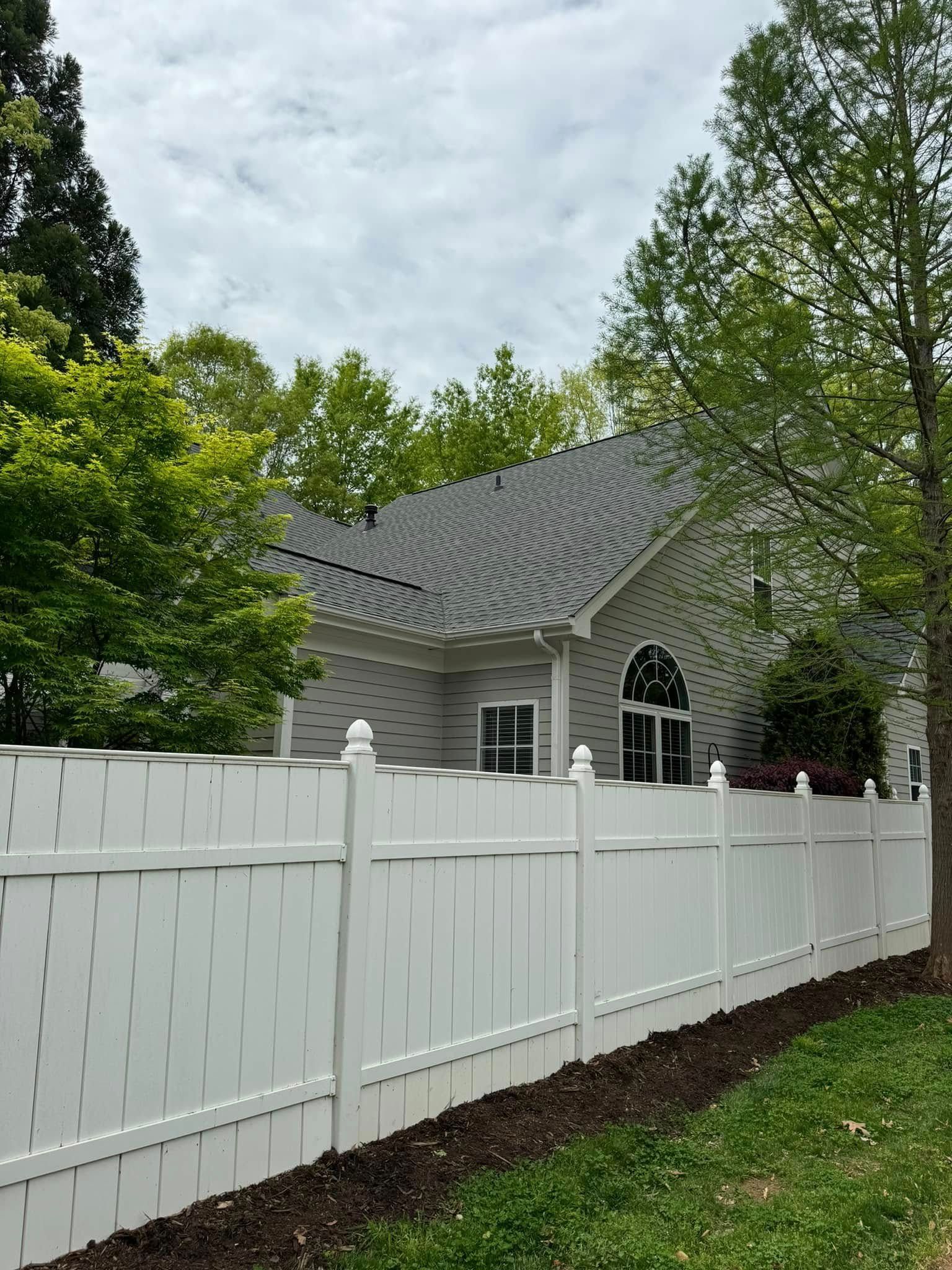A white fence surrounds a house with a gray roof.