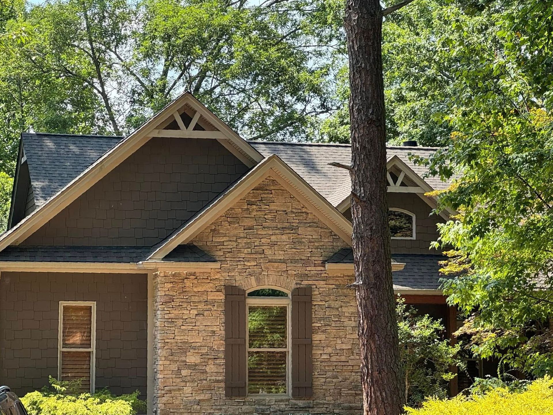A large stone house with a roof and shutters is surrounded by trees.