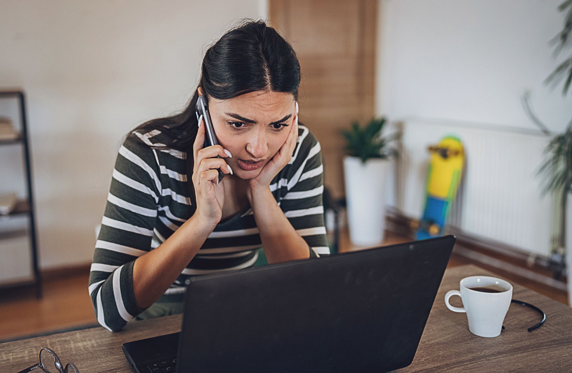 A woman is talking on a cell phone while using a laptop computer.