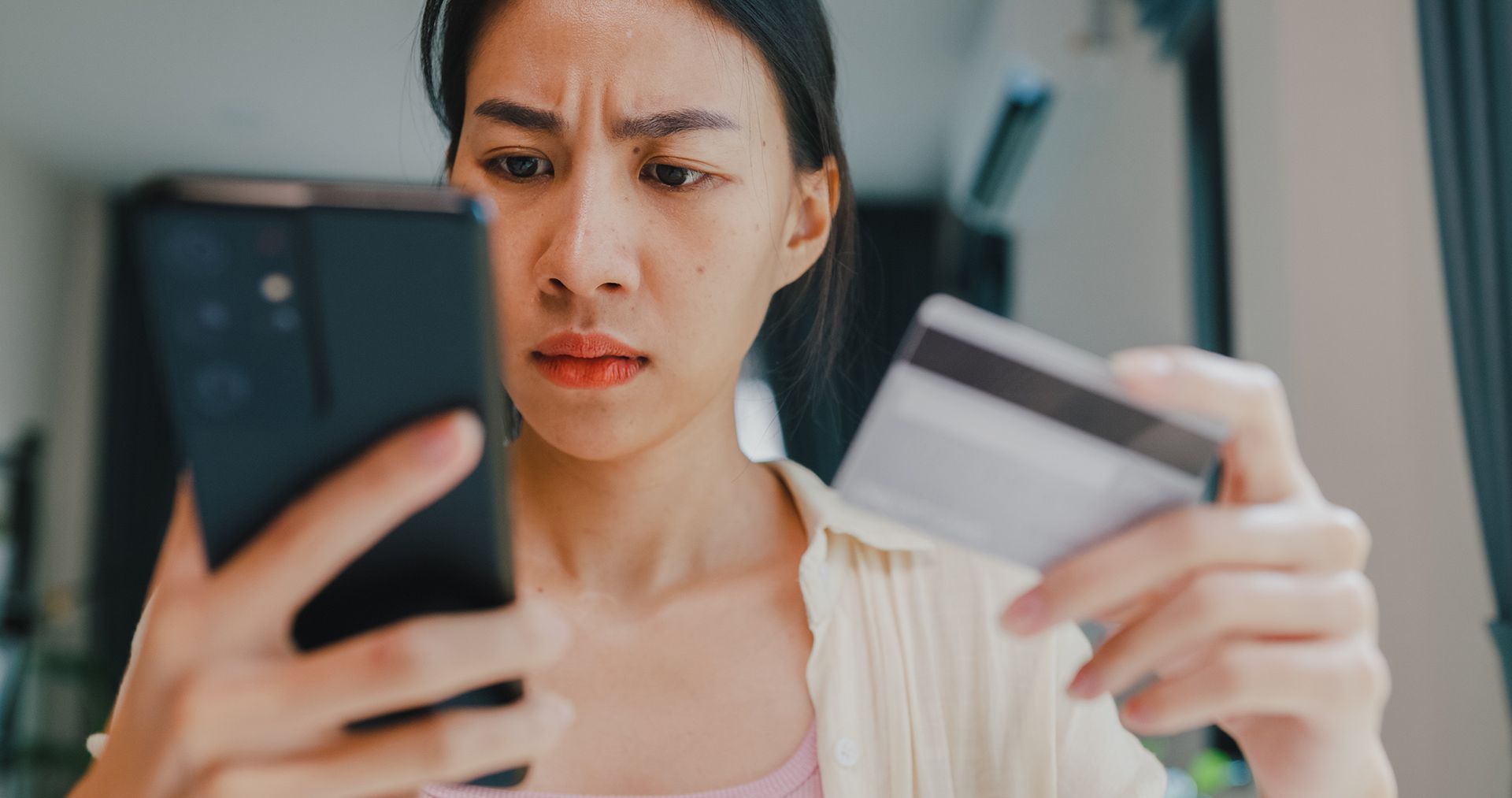 A woman is holding a credit card and looking at her phone.