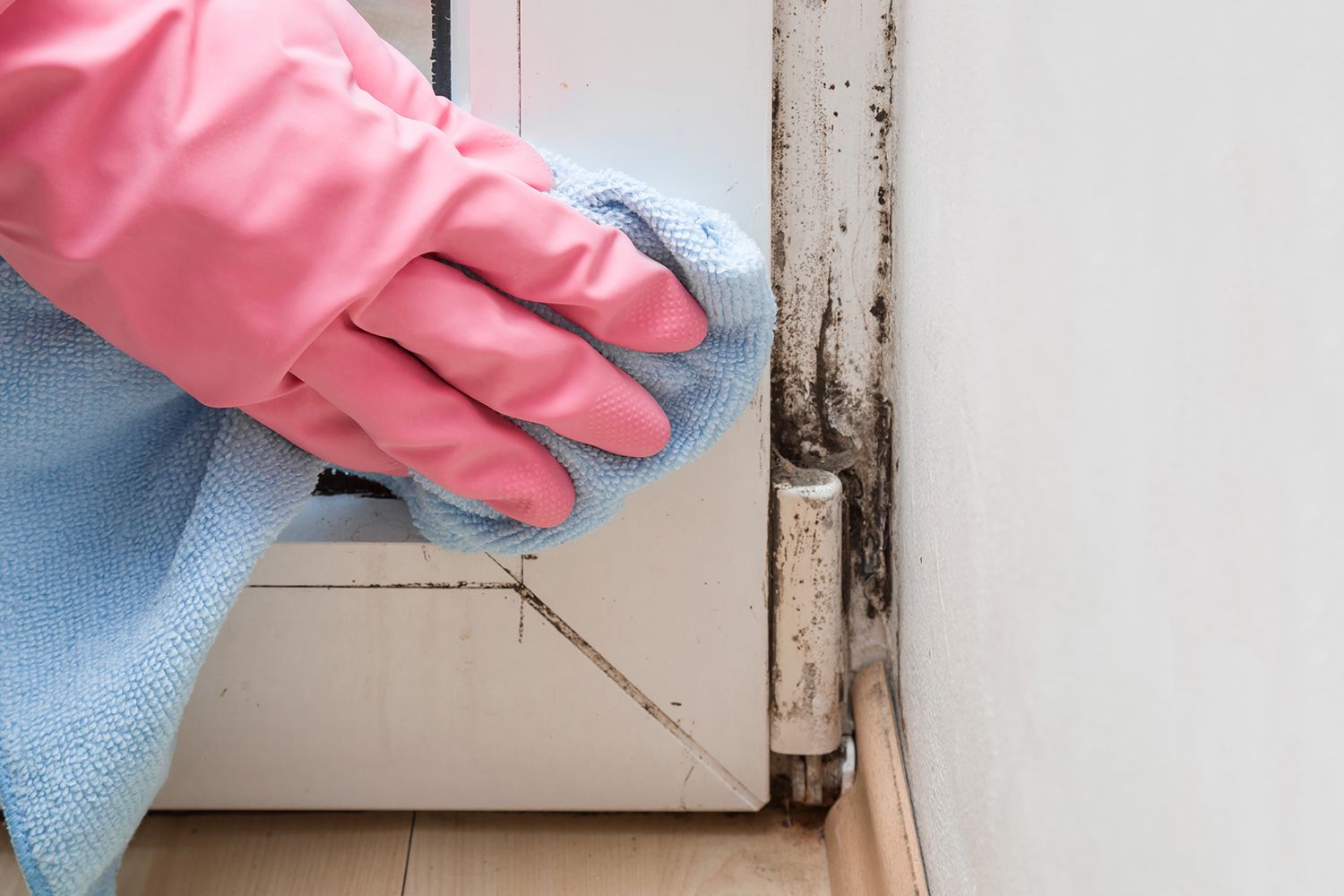 Gloved hand wiping mold from a door frame with a cloth during detailed cleaning.