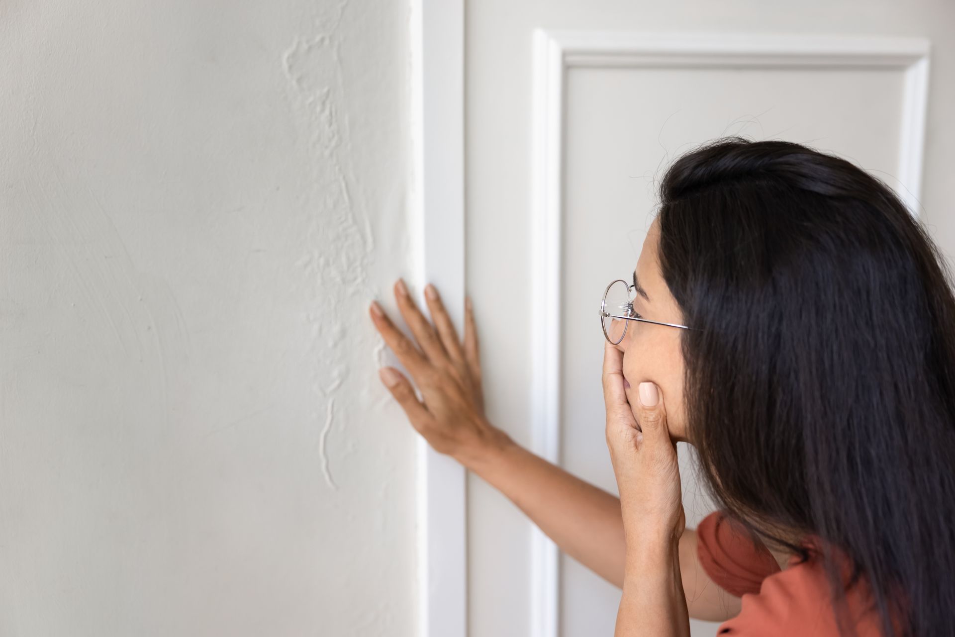 Person inspecting peeling and water-damaged wall paint beside a doorway indoors. Person inspecting peeling and water-damaged wall paint beside a doorway indoors.