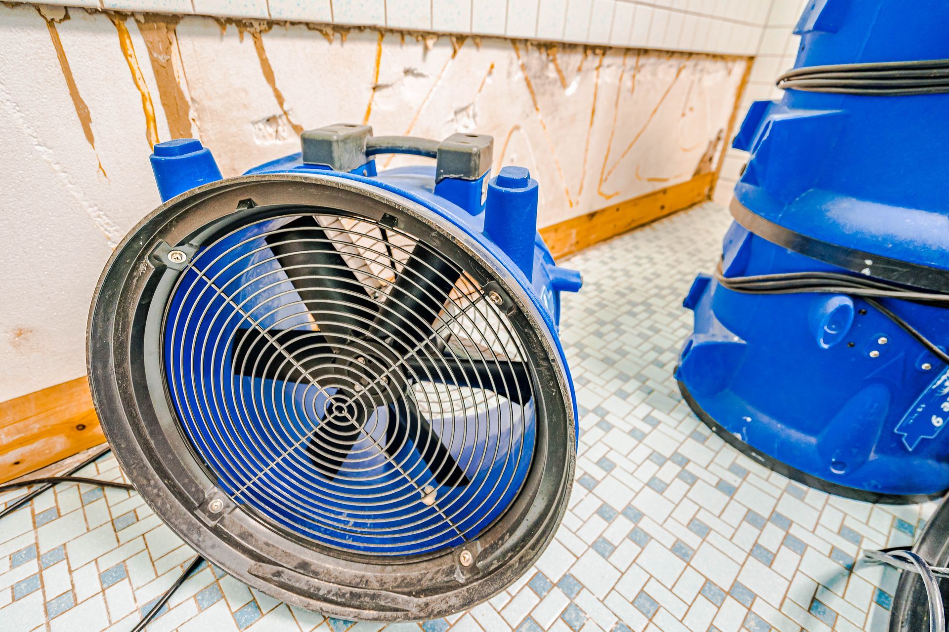 A blue industrial air mover drying a tile floor after water damage.