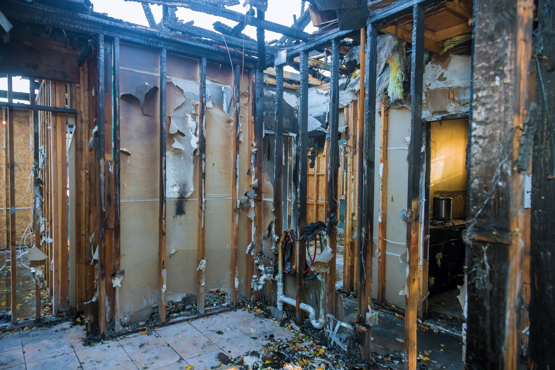 Interior of a room destroyed by fire; charred walls, exposed studs, debris on floor.