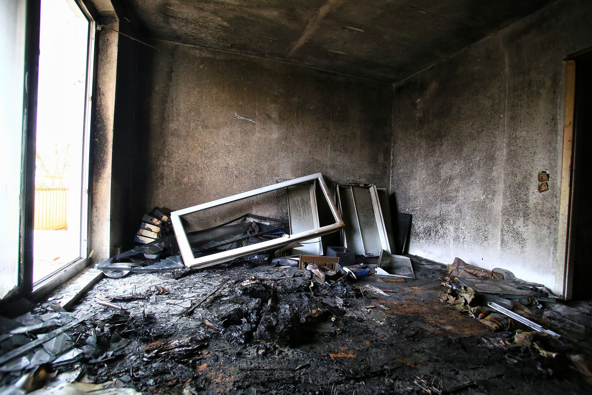Interior of a room destroyed by fire; charred walls, debris, and a broken window frame.