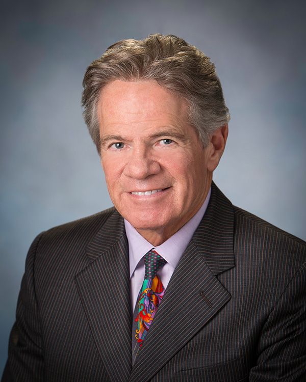 Smiling older man in a suit and patterned tie, head and shoulders portrait.