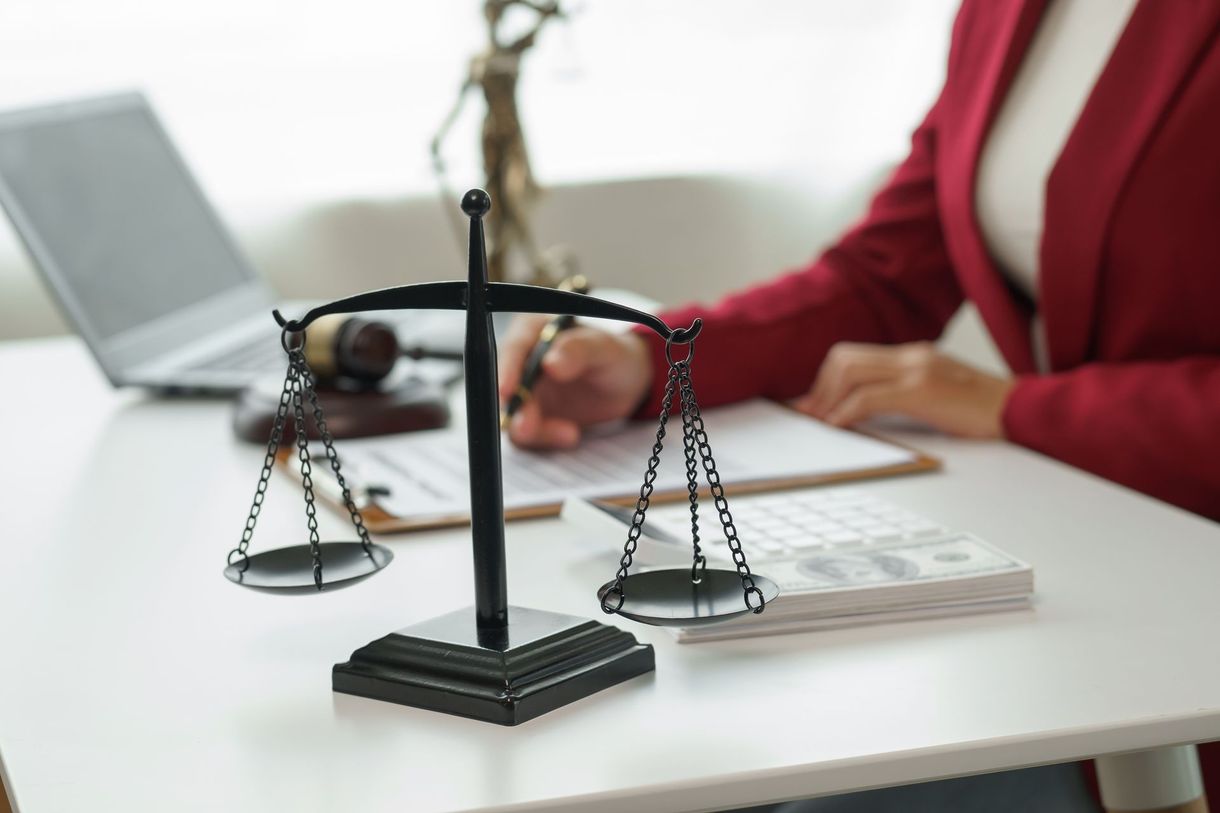 A woman is sitting at a desk with a scale of justice and a statue of justice.