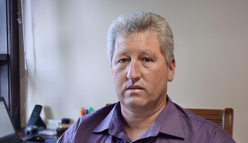 Um homem de camisa roxa está sentado em uma mesa em um escritório.