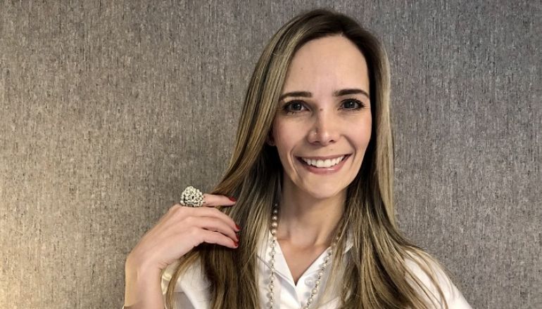Uma mulher de camisa branca está sorrindo e segurando o cabelo.